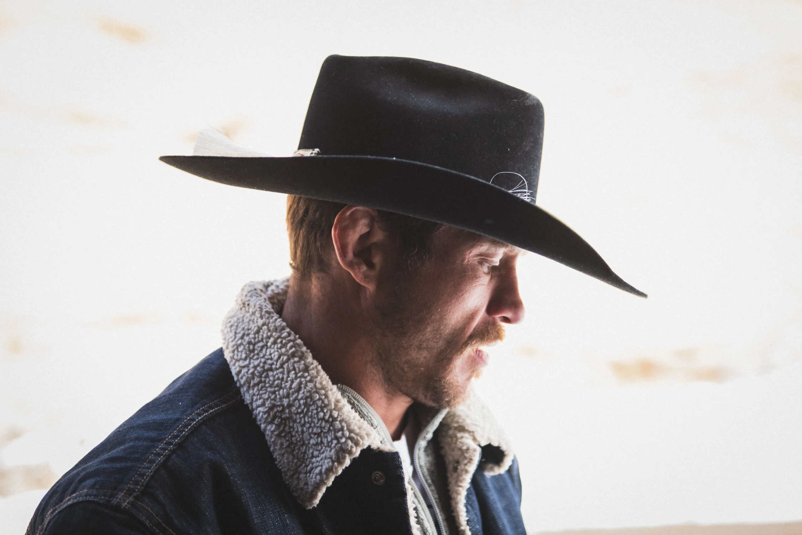 Cowboy figure wearing black hat and fur-lined jacket, looking to the side