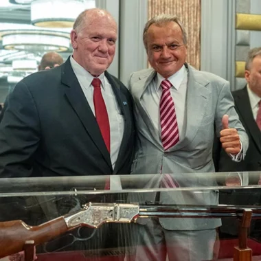 Two men in suits standing in front of display of firearms at a Henry Repeating Arms event