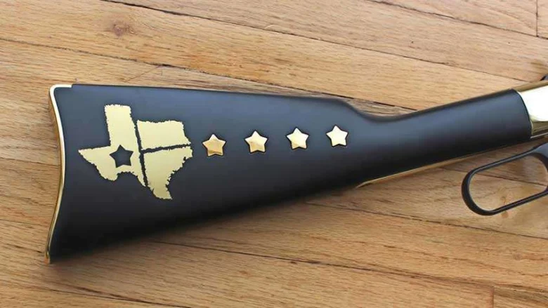 Black gun stock on a wooden surface featuring a gold Texas outline with a star and four gold stars in a row, decorative patriotic design.