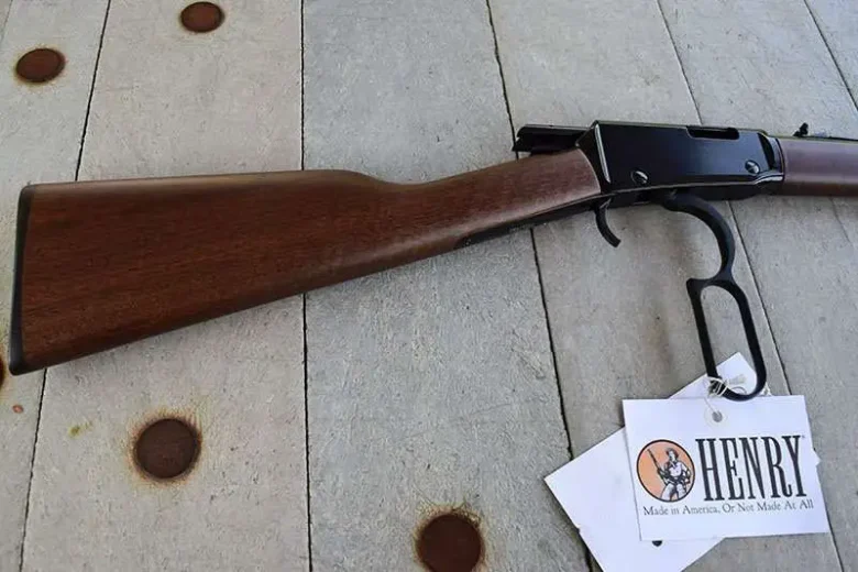 Lever-action rifle with wooden stock resting on a wooden surface, Henry brand tag attached to trigger guard