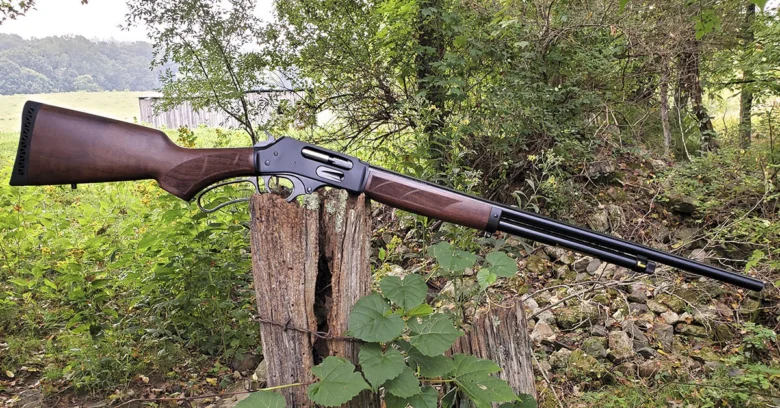 Lever-action rifle with a wooden stock propped on a weathered fence post in a grassy, rural area outside.