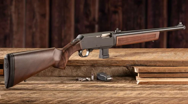 Bolt-action rifle with wooden stock resting on a workbench, with ammo and parts nearby.
