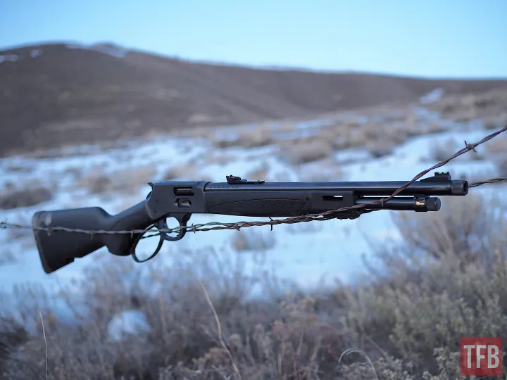 Bolt-action rifle perched on barbed wire in a snow-covered landscape with hills in the background