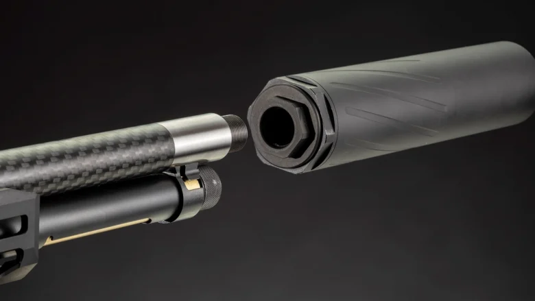Close-up of a rifle barrel attaching a suppressor, showing threading and mounting collar.