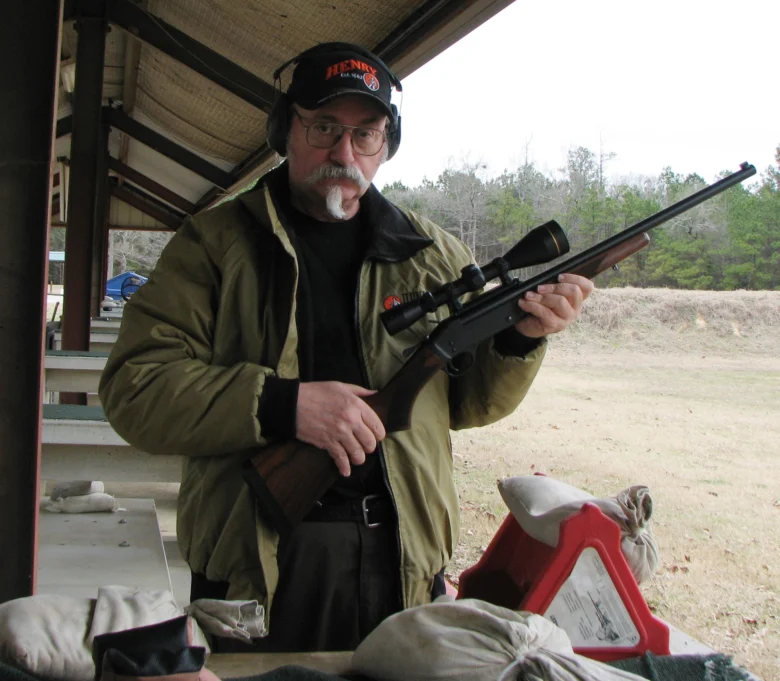 Man holding a lever-action rifle while standing on a porch, surrounded by the outdoor environment