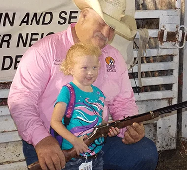 A man in cowboy hat and daughter with rifle, bonding over shared outdoor interests