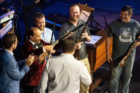 Speaker in red suit addressing audience of veterans and supporters at event