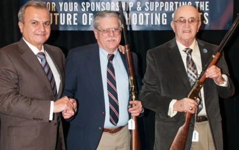 Three men in suits standing together and shaking hands at an NRA event