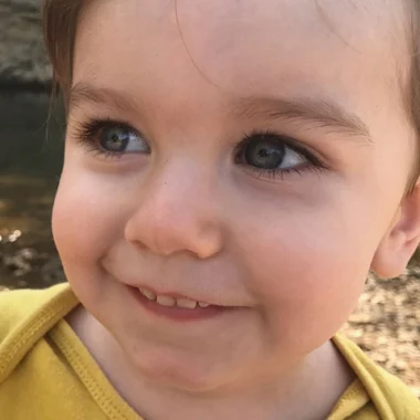 Portrait of a smiling young child with blue eyes and a yellow shirt against a natural background